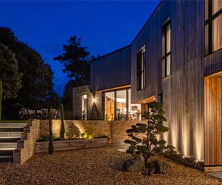 exterior of timber clad modern home with lighting set in planters and on exterior walls