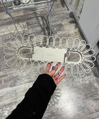 A white woman's arm in a black knitted sweater, holding a cream Petal hanger which is a rounded plastic gadget with metal hooks and plastic rounded petal shape sections for holding socks