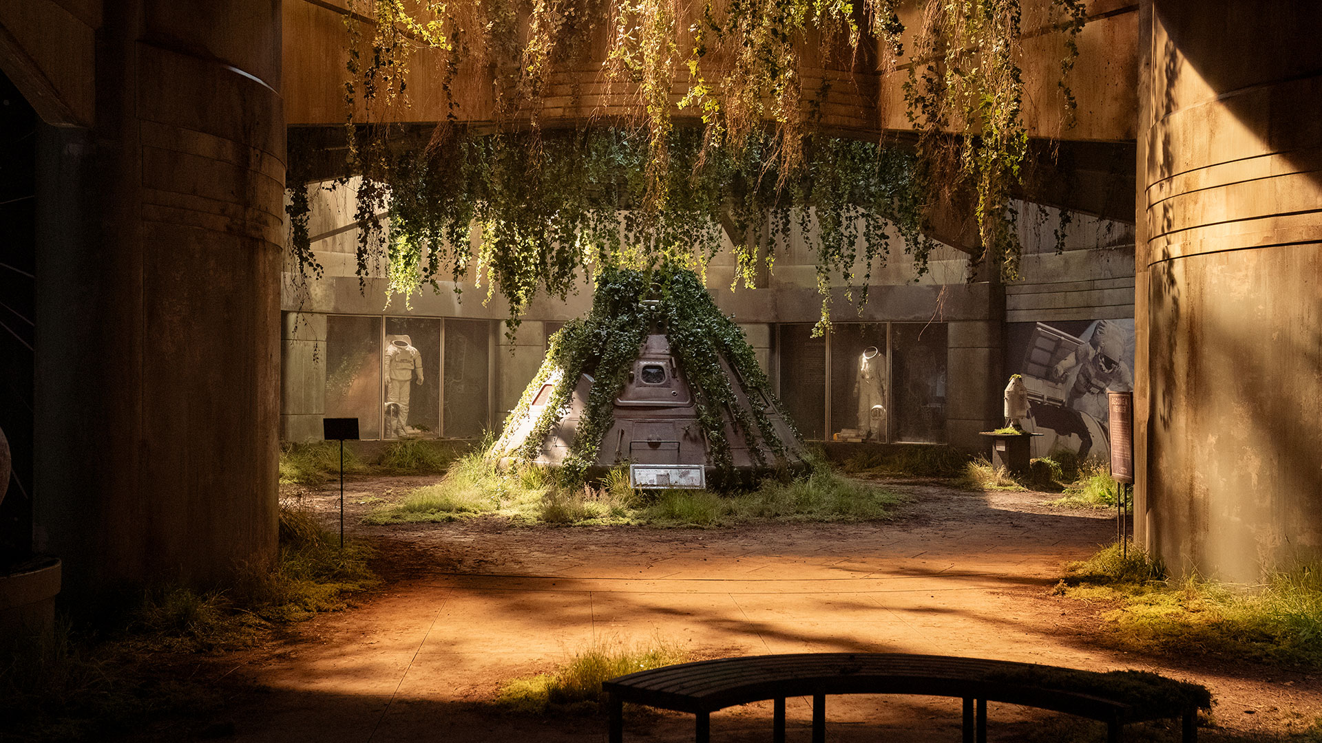 a photograph of a television set with a space capsule overgrown with plant vines at its center and spacesuit displays in the background