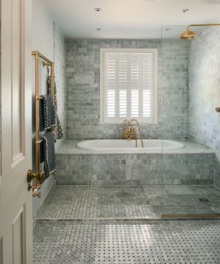 Gray wetroom with shower, tiled bathtub, flooring and walls. Gray tiles of different shapes and sizes, metallic fittings,