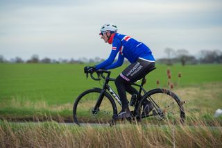 Adam Jones in blue Manchester Wheelers kit riding a bike with a field in the background
