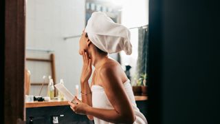 woman in towel applying lotion to neck