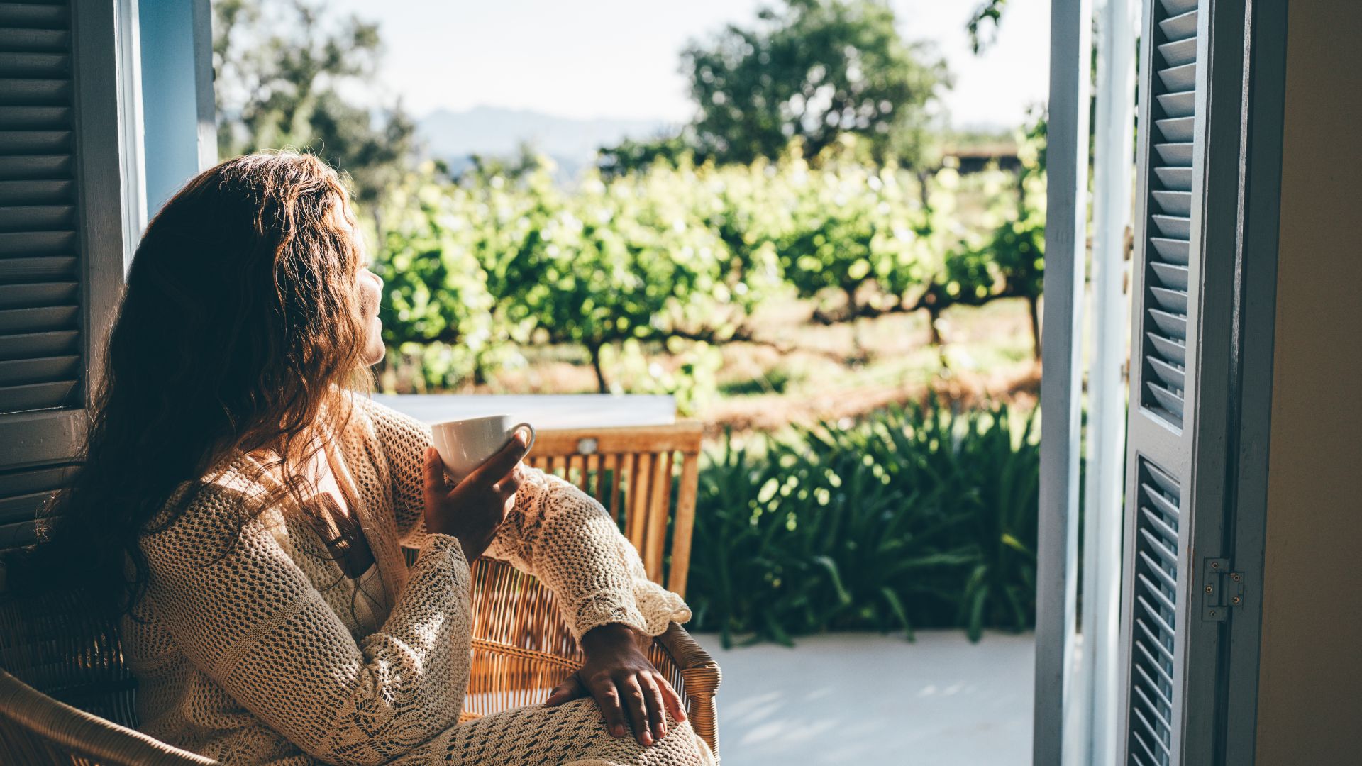 A woman with auburn hair sits in her bedroom overlooking a field.