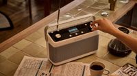 A white Roberts Stream 219 radio on a kitchen table with a hand touching the controls.