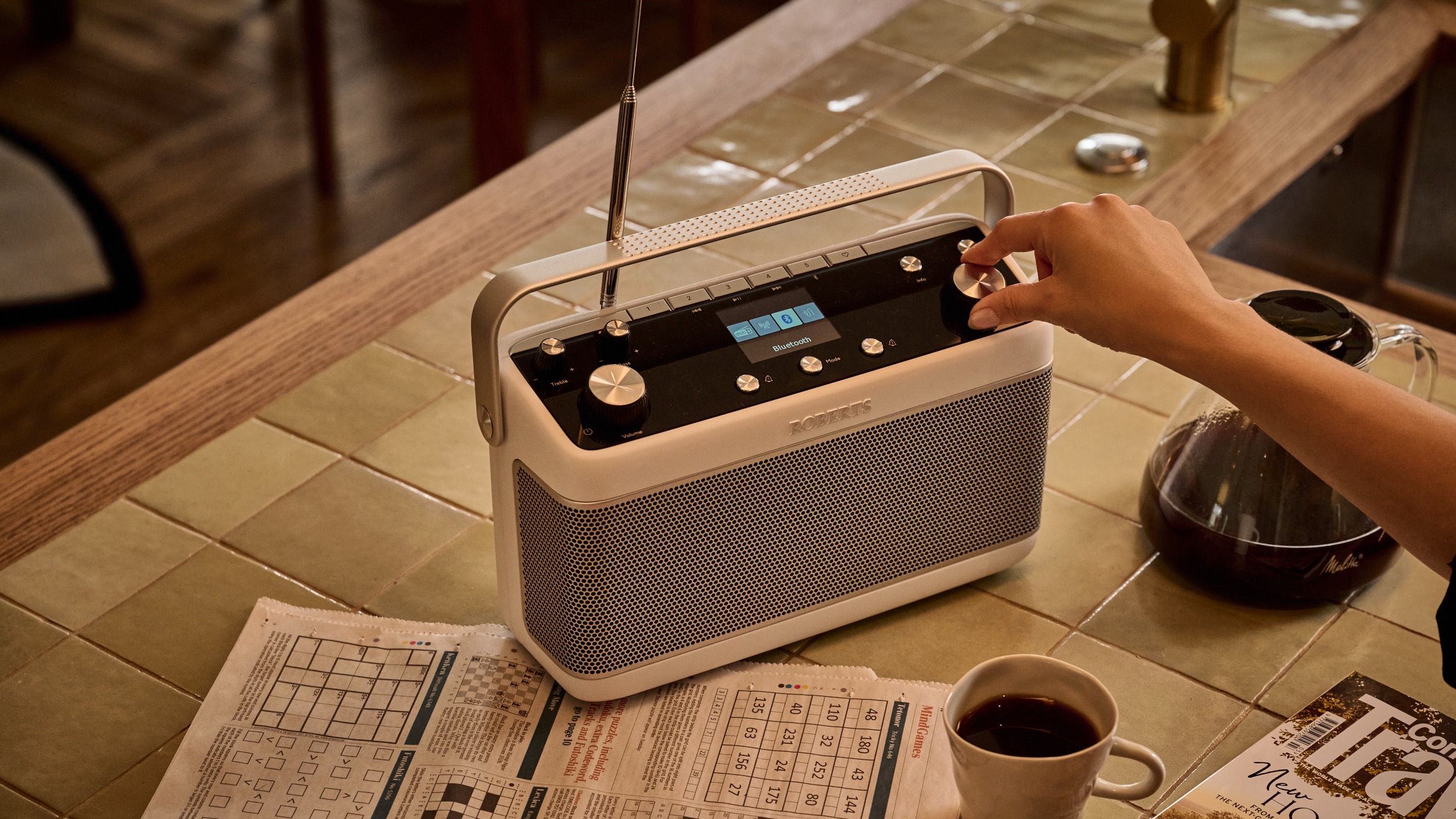 A white Roberts Stream 219 radio on a kitchen table with a hand touching the controls.
