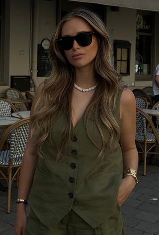 a close photo showing what to wear to the office in the summer with a woman wearing a green linen suit vest with matching shorts, gold bangles, and a pearl necklace