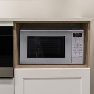 silver microwave under kitchen counter on top of white cupboard