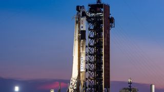 a white rocket stands upright on a launch pad at sunset