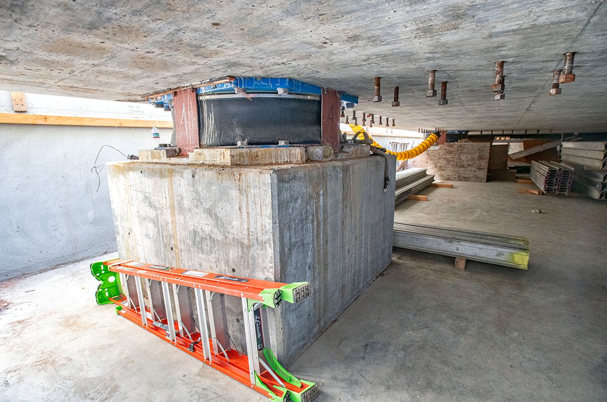 a black cylinder rests atop a concrete cube, with an orange ladder on the ground nearby