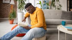 A young man is intensely focused on reading a book in his living room.