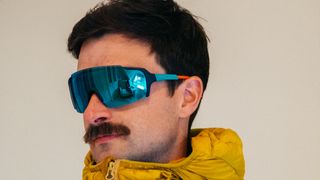 A white man with a moustache wears a pair of monolens sunglasses