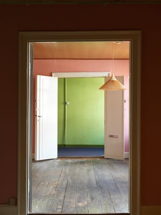 A view through a doorway of another doorway with white double doors and a green wall behind it.