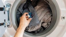 Someone putting a laundry pod into a white washing machine with a full load of laundry