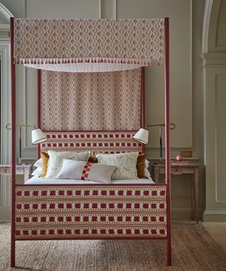 colors that go with red, bedroom with light grey walls, red metal four poster bed with fabric canopy and upholstered headboard, matching nightstants with table lamps, jute rug,