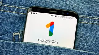 The Google One logo displayed on a smartphone screen that is sticking out of a pocket on a denim item of clothing.