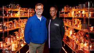 Hugh Dennis and April Jackson standing side by side, superimposed on a black background with rows of pots and pans behind them.