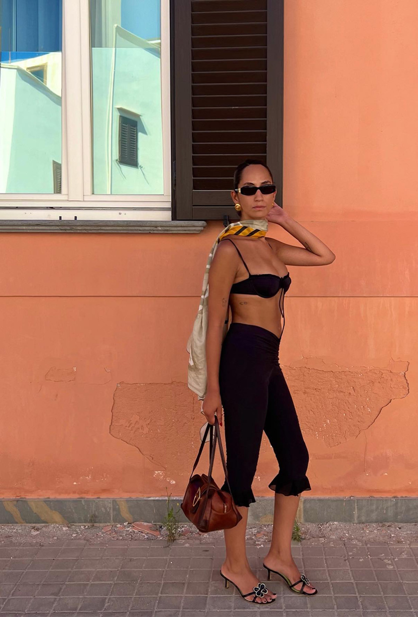 How to pack for Italy is shown in a picture of a woman wearing a black bikini top, black capri pants, and black heeled sandals