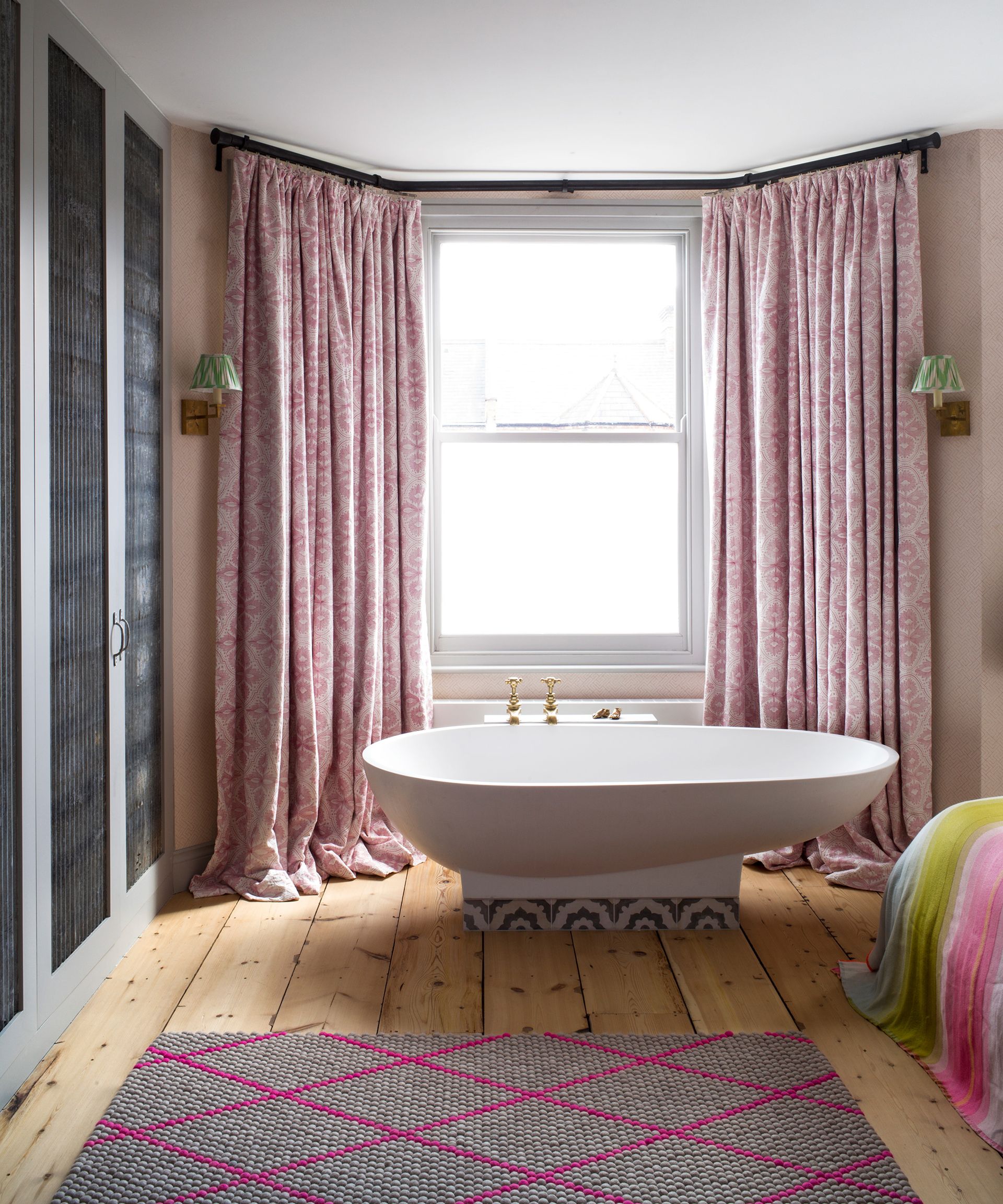 A white free standing bath in a bedroom with pink curtains