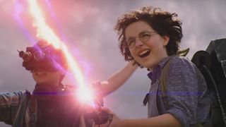 Phoebe (McKenna Grace) and Podcast (Logan Kim) fire a proton pack in Ghostbusters Afterlife