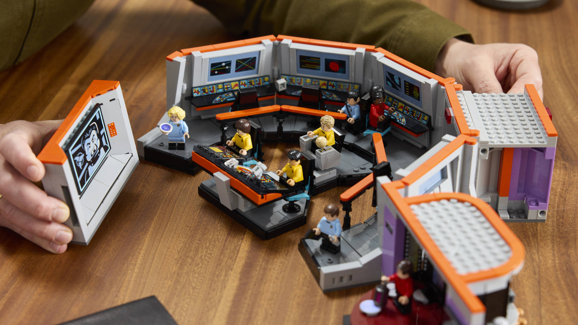 Hands place panels for the Lego Star Trek Enterprise Bridge into position as the set sits on a wooden table
