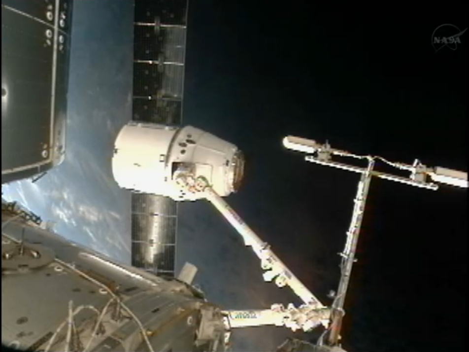 The blue Earth glows behind SpaceX&#039;s private Dragon spacecraft as it sits at the end of the International Space Station&#039;s robotic arm.