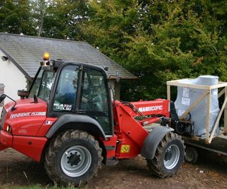 red and black forklift truck with wrapped boiler being offloaded from a delivery truck