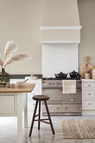Rustic cream kitchen ideas with stainless steel range cooker, wooden stool and large vase of feathery grasses.