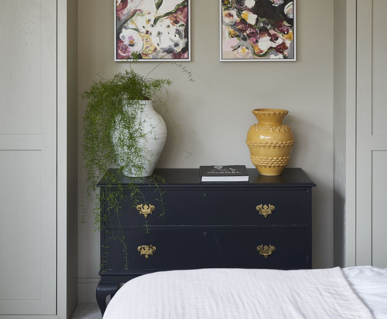 A bedroom with a navy set of drawers in an alcove decorated with vases