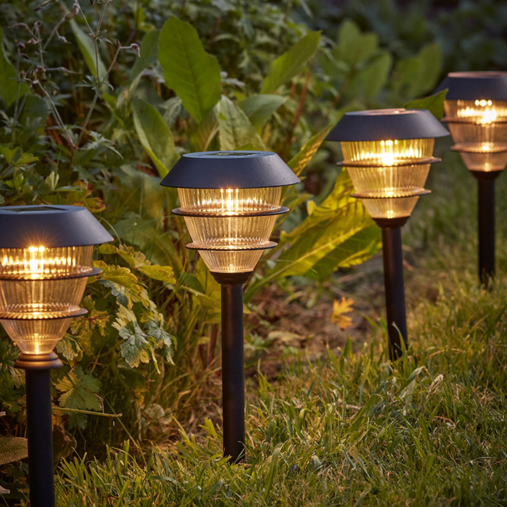 Four black solar powered stake lights in the grass lit up