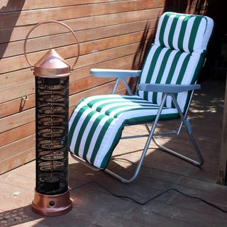 The Kettler Kalos copper lantern patio heater being tested on wooden decking next to a green and white striped chair