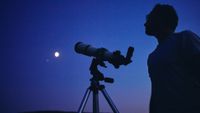 Telescopes at Walmart: Image shows man standing next to telescope looking at moon 