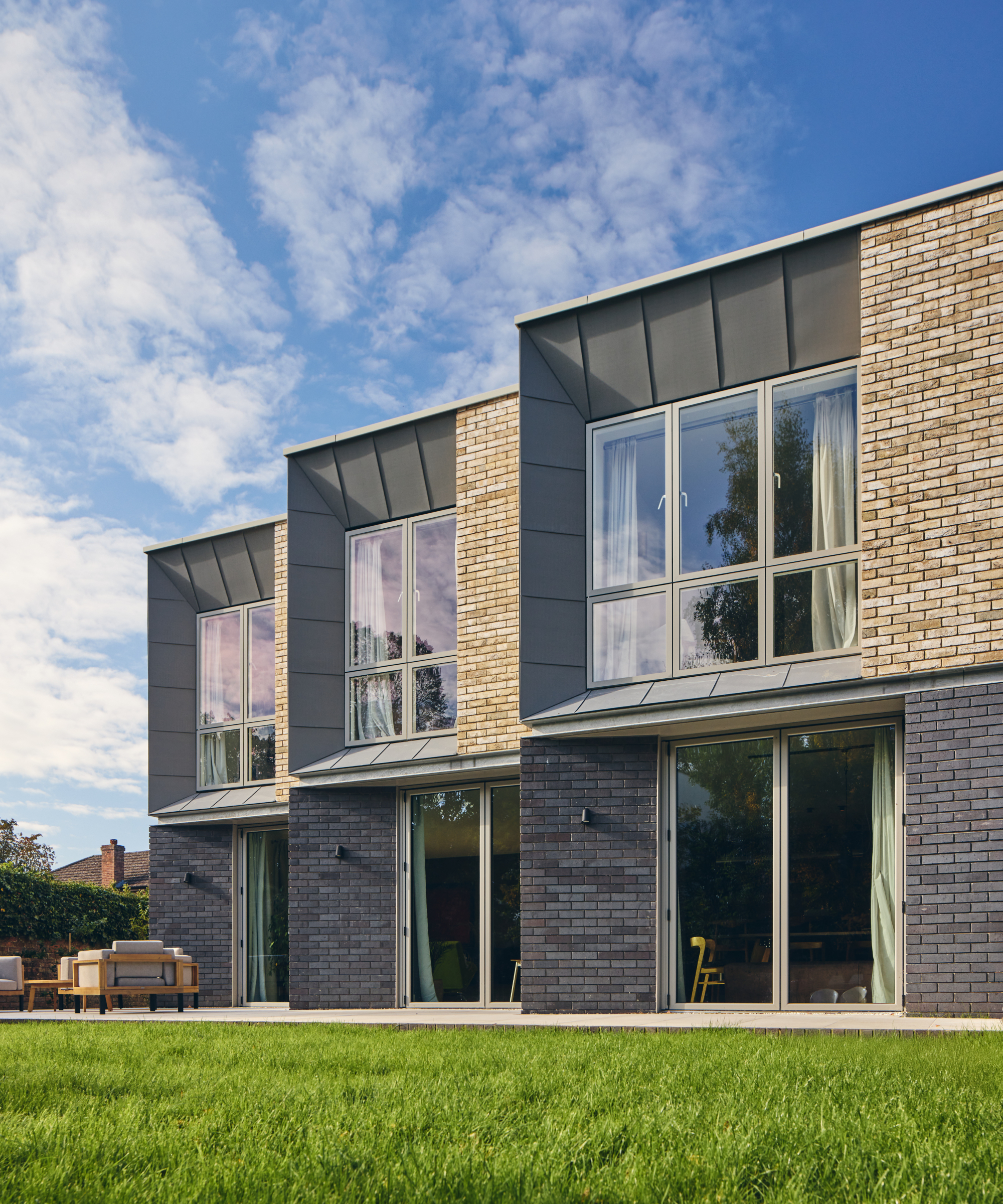 contemporary home clad with pale bricks, zine panels around windows on second storey and slate on lower level, large sections of windows on top level and doors on lower level