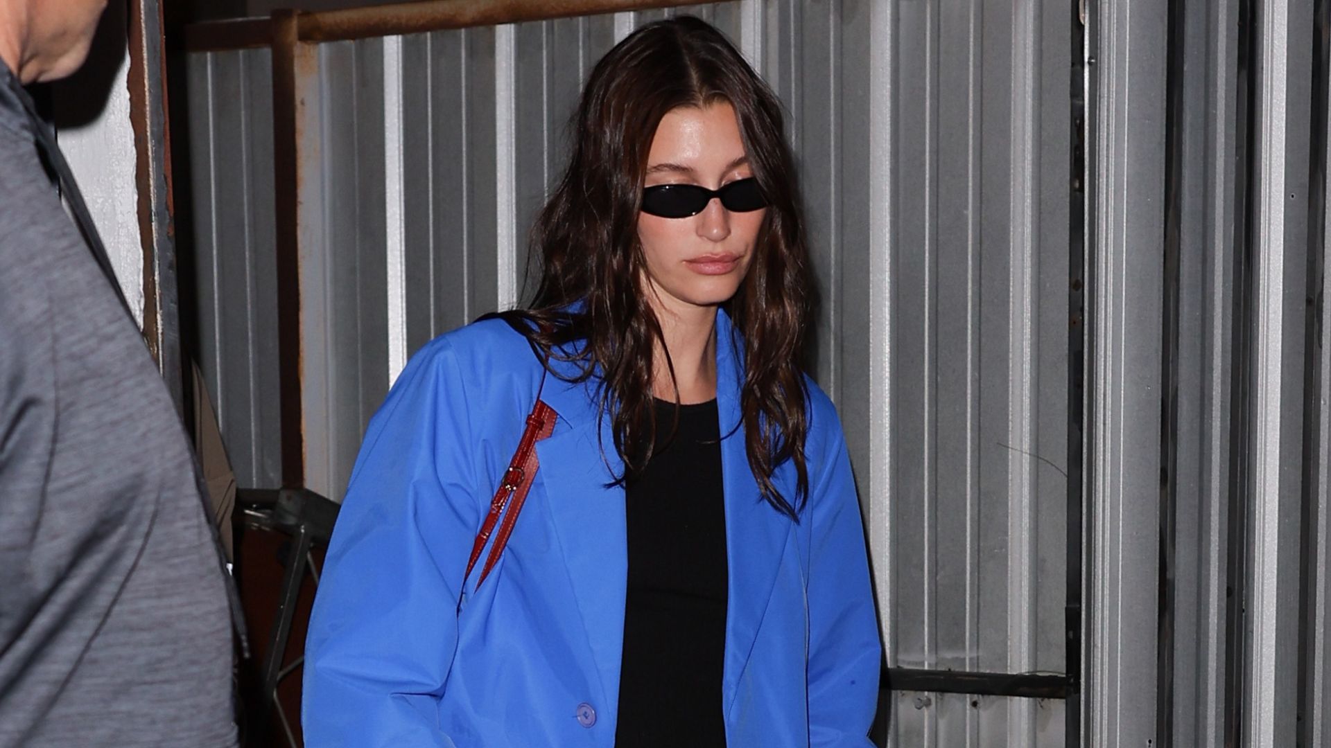 Hailey Bieber steps out wearing a cobalt blue trench coat with black trousers, a black top and black leather mules.