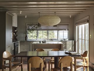 An off white kitchen/ diner with a small island behind the table, and wooden furniture at the table.