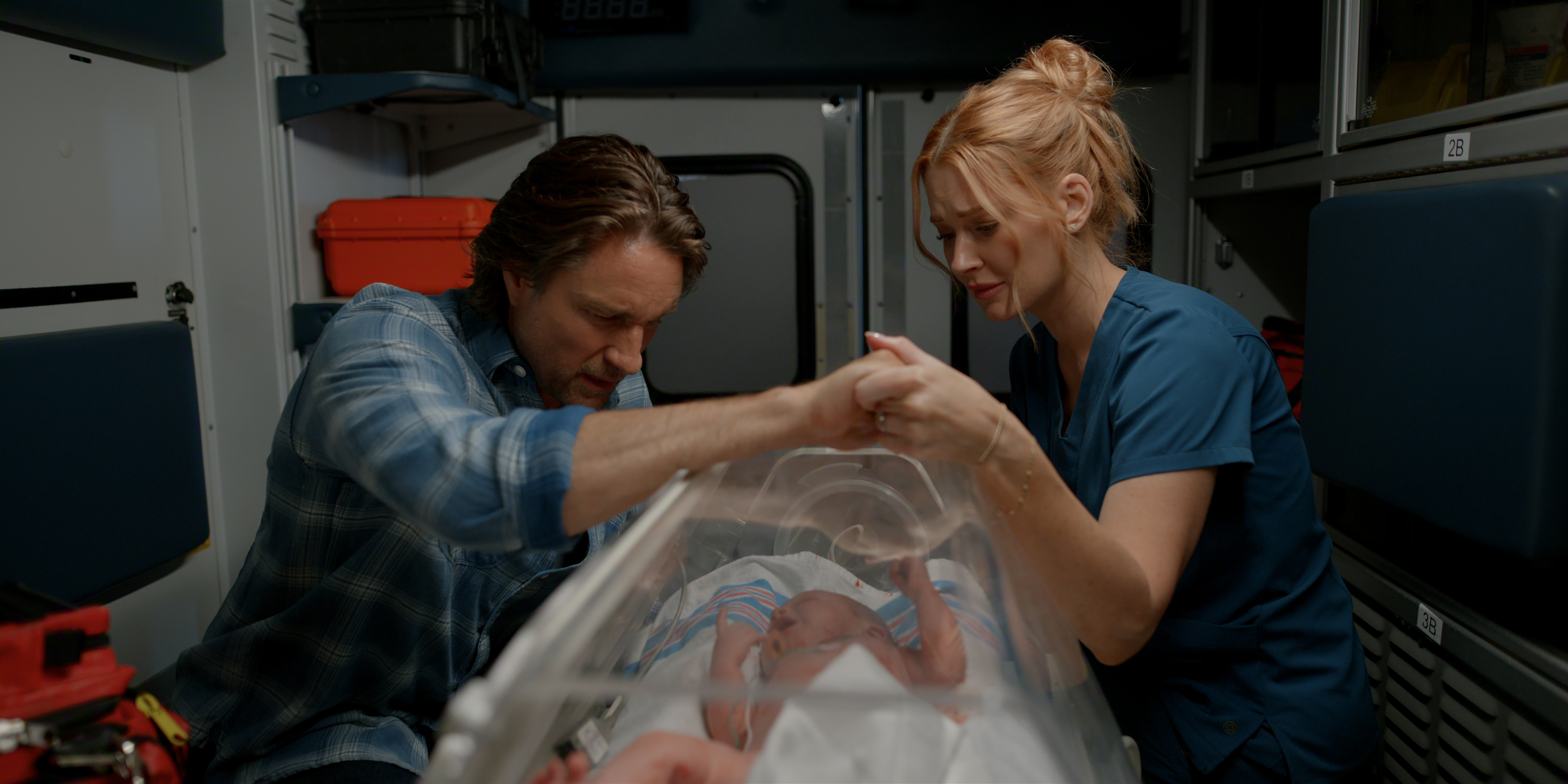 Martin Henderson as Jack Sheridan and Alexandra Breckenridge as Melinda Monroe holding hands over an infant in intensive care at the hospital in a still from virgin river season 7