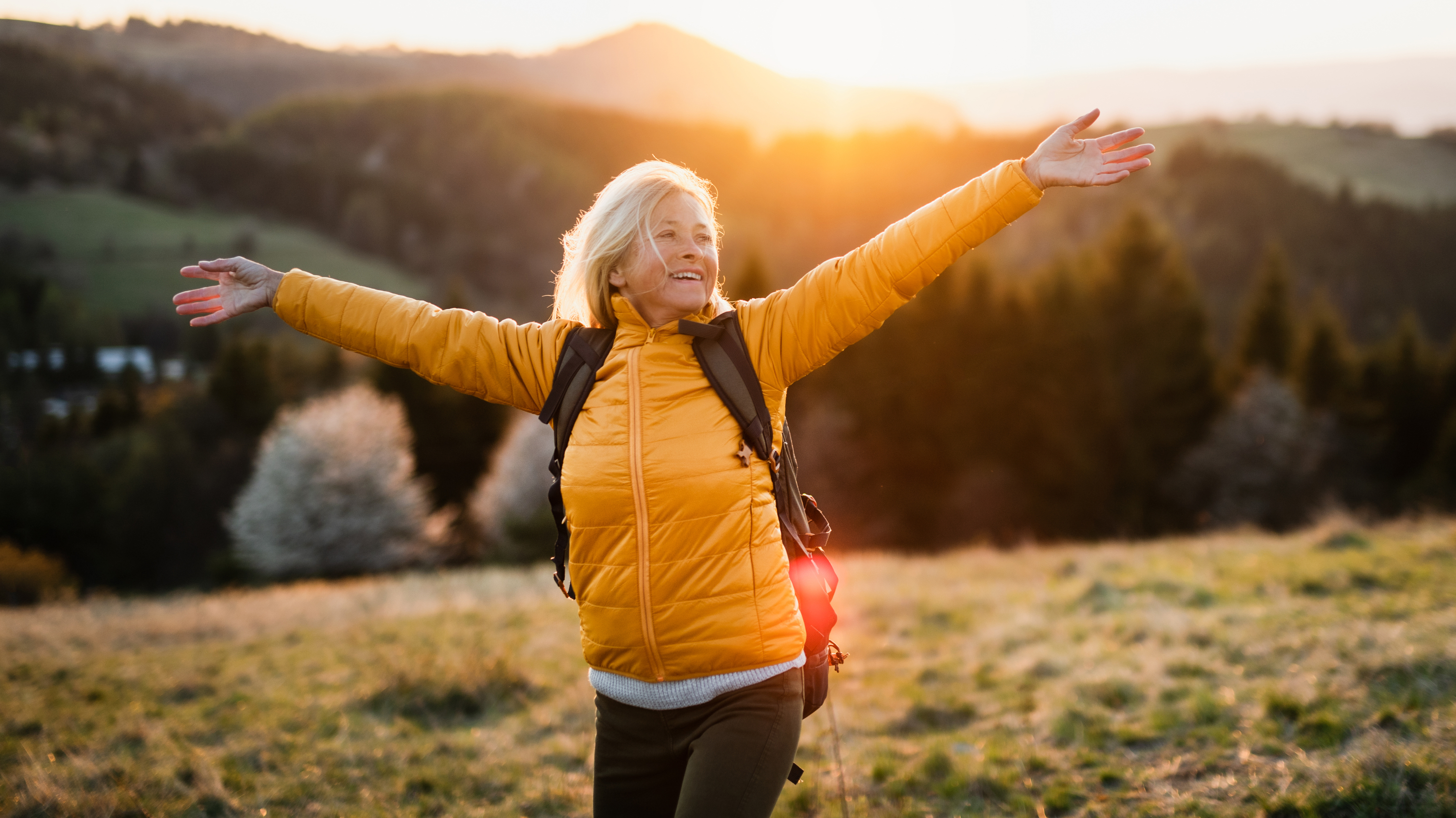 a woman with her arms open basking in the sunshine on a hill