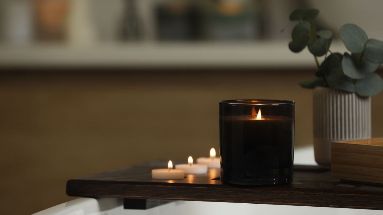 A jar candle and tea lights on a bath tray in a dark bathroom