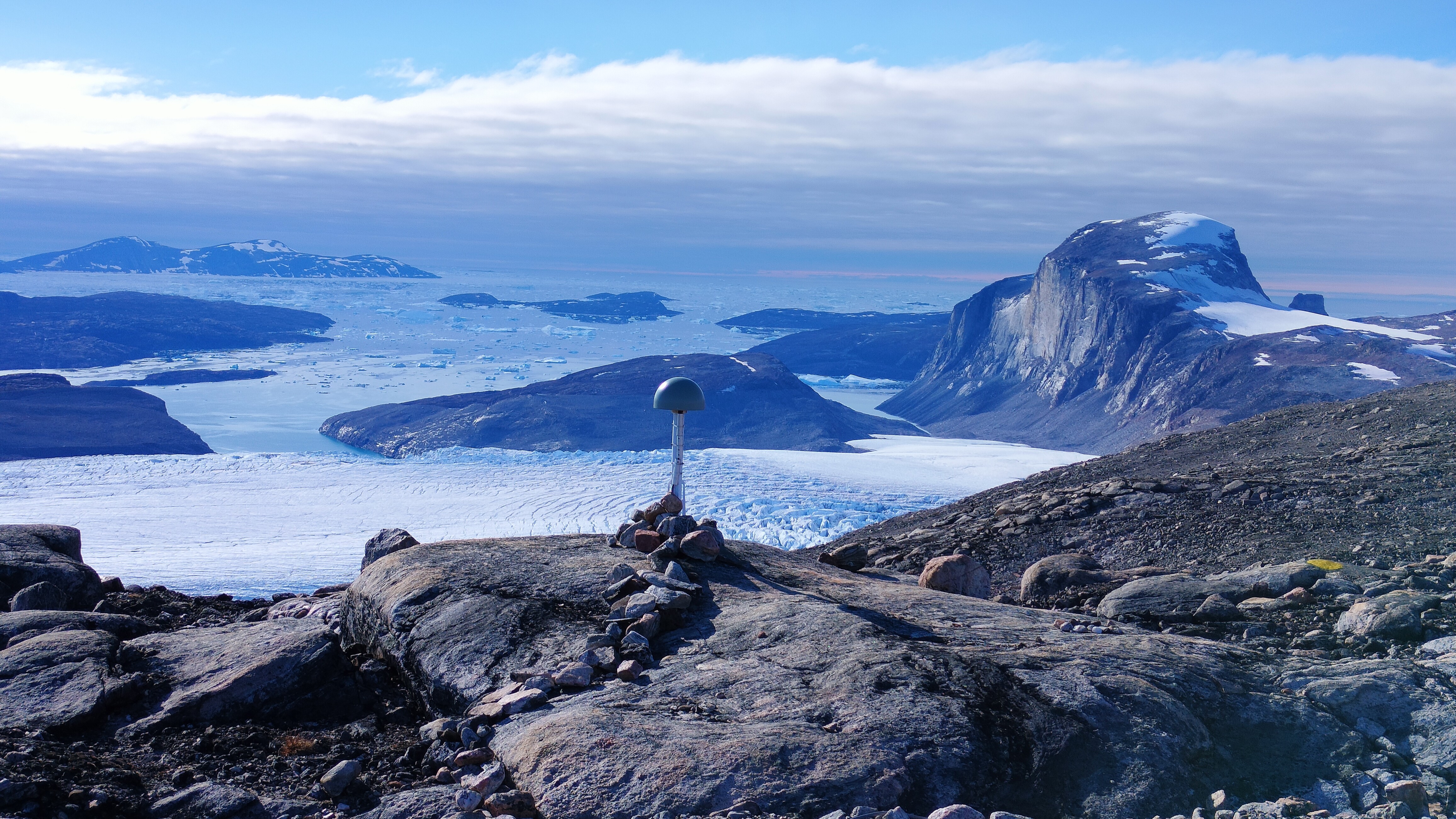A satellite station in Greenland. We see the station on an outcrop and the ice sheet in the background.