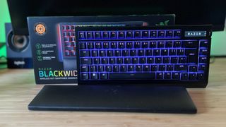 Razer BlackWidow V4 Pro 75% gaming keyboard on a wooden desk with packaging and wrist rest