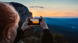 Woman using iPhone to photograph landscape at sunset