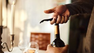 person opening wine bottle with corkscrew