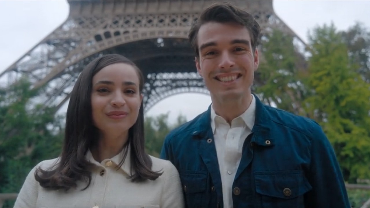 From left to right: Sofia Carson and Corey Mylchreest smiling under the Eiffel Tower.