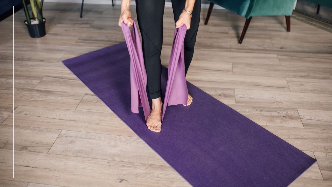 Woman standing on a yoga mat at home on hardwood floor, using resistance band under foot in full-body resistance band workout