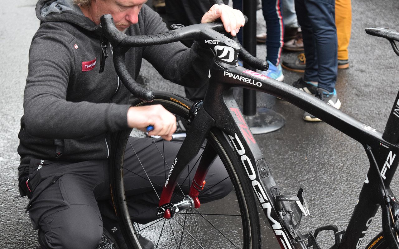 A Team Ineos mechanic adjusts the brakes of all team riders' bikes ahead of the start on a wet Stage 2