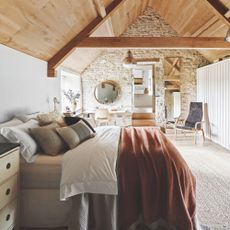 Large loft conversion bedroom with exposed beams and brickwork, with pillows and throws on the bed