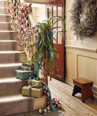Hallway with wooden floor, wood banisters and panelled wall, paper chains decorating the banister, large wreath on the wall and gift wrapped presents on the stairs.