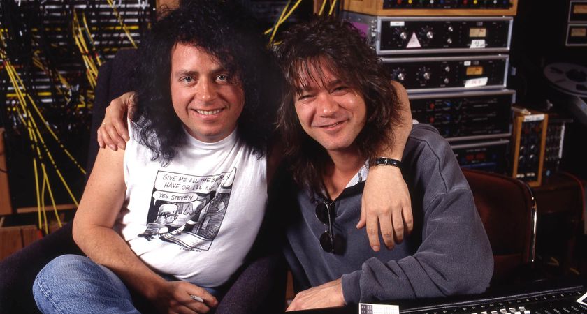 Steve Lukather and Eddie Van Halen pictured in the studio together. Lukather wears a white sleeveless T-shirt. Van Halen wears a grey longsleeve. Studio equipment can be seen in the background.