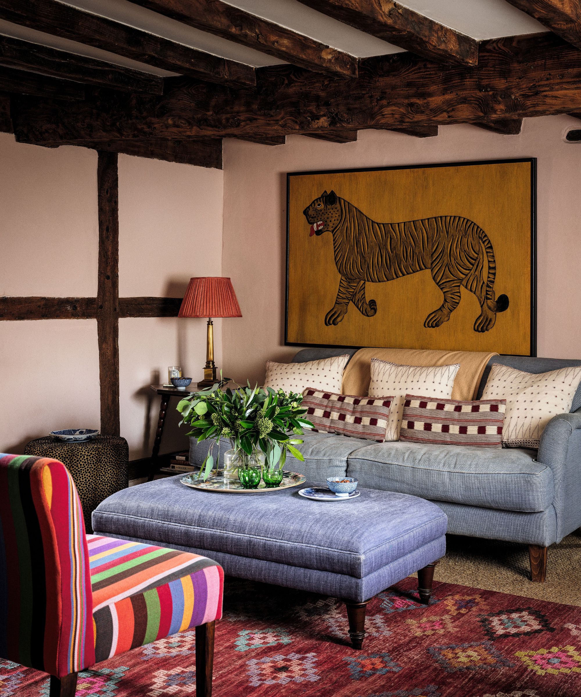 Cozy seating area with wooden beams and a tiger print on the wall. There's a gray sofas and ottoman and a colorful stripe print chair