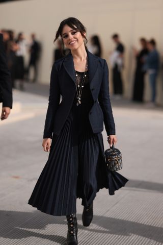 Jenna Ortega mengenakan blazer denim Dior, rok midi, dan tas rias bermotif pada pertunjukan Dior musim semi musim panas 2024 di Paris.