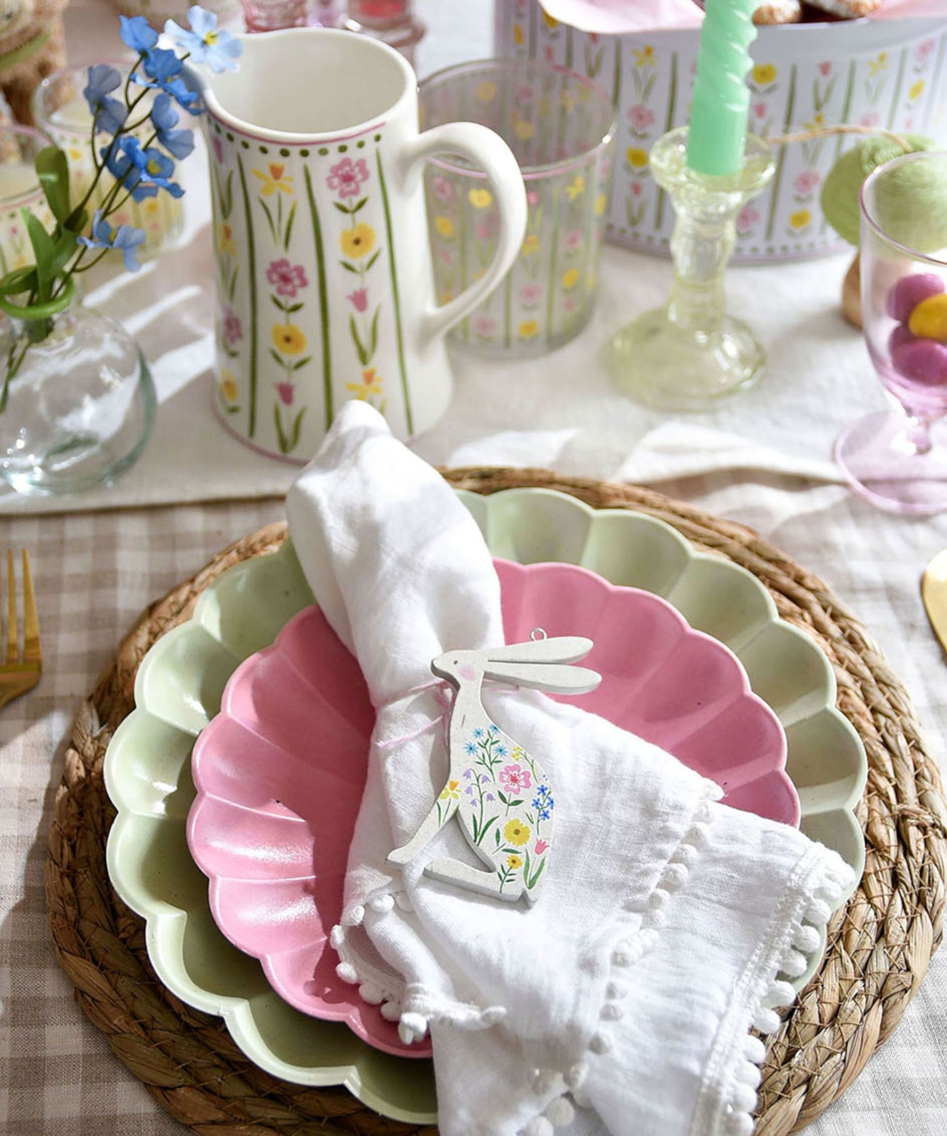 Easter table with gingham tablecloth, rattan placemat, green and pink plates and white linen napkin with bunny napkin ring